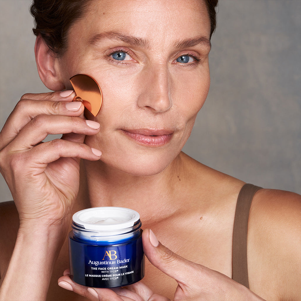 woman applying augustinus bader the face cream mask to her face
